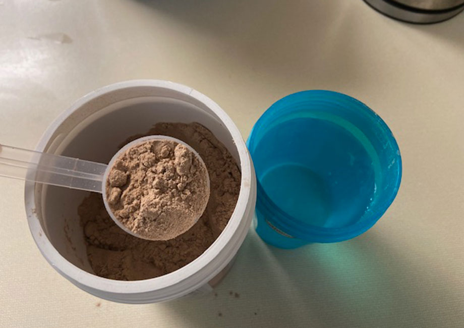 Lifting a scoop of Tone It Up Protein from the container.