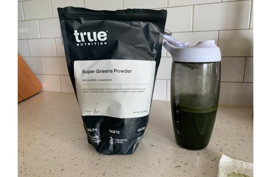 a bag of true nutrition super greens next to a white shaker cup