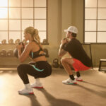 Two people squat with kettlebells while wearing Reebok Nano X5