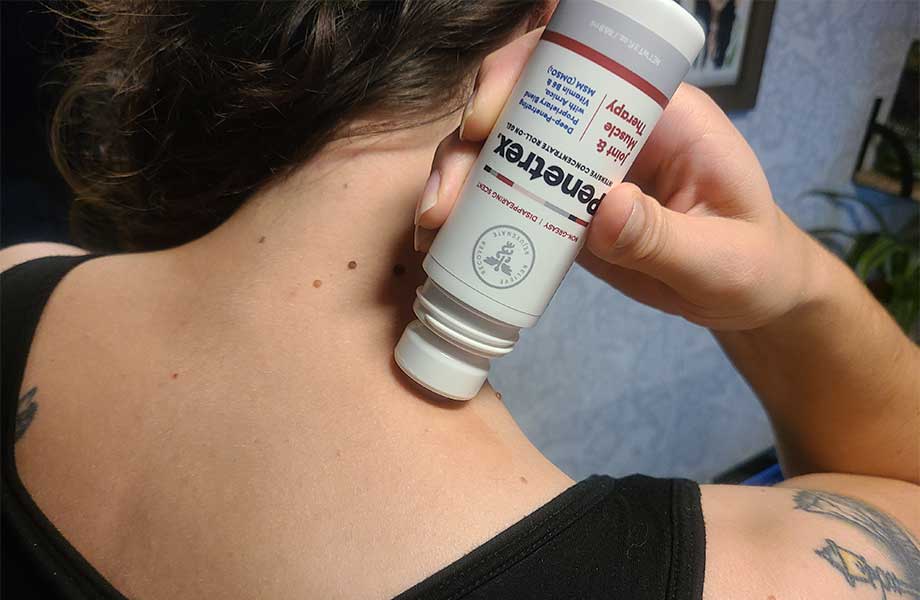 A person applies Penetrex Pain Cream to their shoulder with the roll-on bottle.