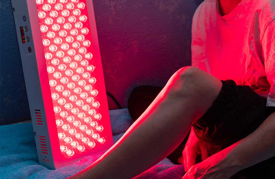 A close look at someone using a red light therapy device on their leg.