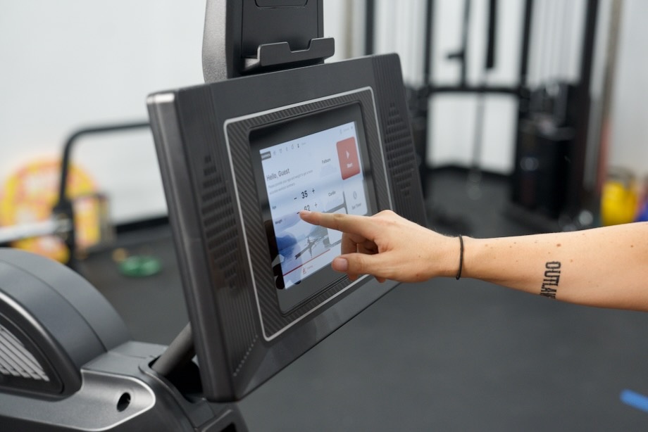 A hand interacts with the touchscreen from a Sole SR550 rowing machine