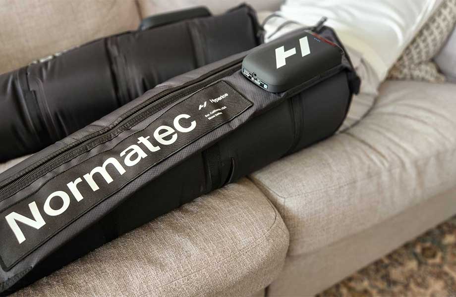 A pair of Normatec Elite Recovery Legs being used on a couch.