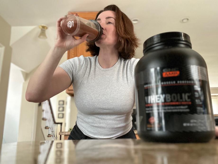 A woman is drinking some GNC AMP Wheybolic Protein.