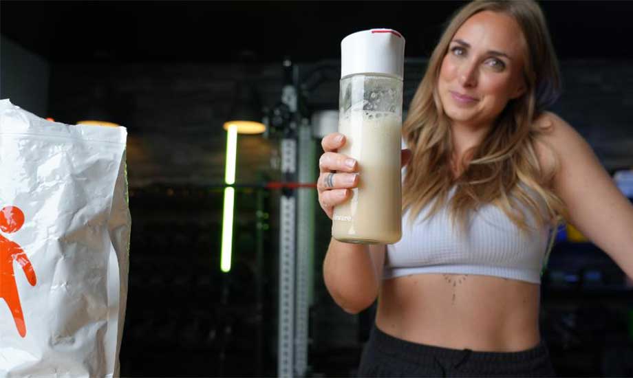 A woman holds up a shaker glass of Bulk Supplements Soy Protein.