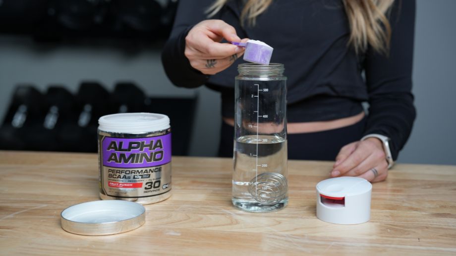 Woman pouring scoop of Cellucor Alpha Aminos into a water bottle